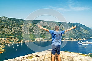 Man tourist standing on Lovcen mountain above Kotor bay and old town and rising his hands, Montenegro. Male traveler