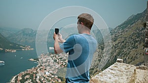 Man tourist taking photo on smartphone standing on Lovcen mountain above Kotor bay and old town, Montenegro. Male