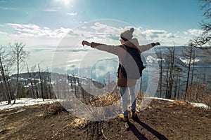 Man tourist traveler stands on a mountain and looks at the beautiful view of lake Baikal. Winter landscape