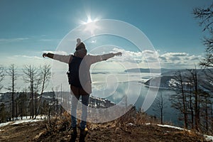 Man tourist traveler stands on a mountain and looks at the beautiful view of lake Baikal. Winter landscape