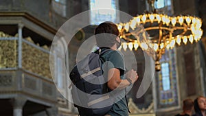 A man tourist, wearing a face mask, stands in awe within the hallowed beauty of Istanbul's Ayasofya, immersed in