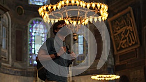 A man tourist, wearing a face mask, stands in awe within the hallowed beauty of Istanbul's Ayasofya, immersed in