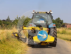 Man in a tractor using a flail to cut grass verges in a country lane. UK