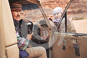 Man in traditional Bedouin coat - bisht - and headscarf, posing behind wheel in old 4wd vehicle, looking to side, younger woman photo