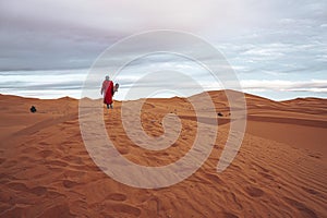 Man in traditional clothes with sandboard standing on sand dunes against sky