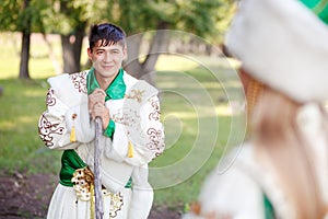 Man in traditional festive dress of steppe nomads, leaned on his cane, looking at wife.