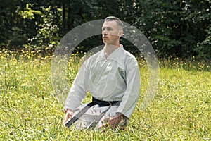 A man in a traditional kimano with a black belt sits and meditates