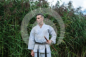 A man in a traditional kimono with a black belt suspiciously listens to silence, among the reeds, prepares for battle