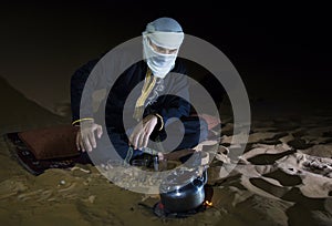 Man in traditional Tuareg outfit making tea in a desert