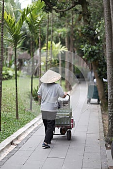 A man in a traditional Vietnamese hat rolls a cart with soft drinks