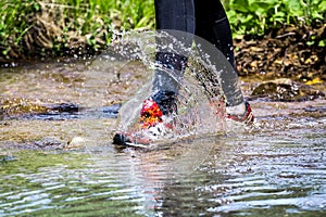 Man trail running in the mountains, crossing a creek