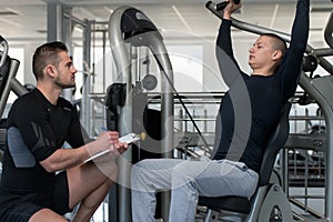 Man Train Chest On Machine With Personal Trainer