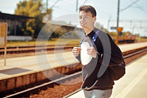 Man on train station, travel. Student in railway station. Smile freelance man. Boy with backpack waiting in a train station in sun