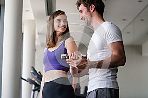 Man trainer flirting with beautiful young woman while helping her at gym