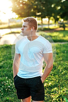 Man trainer in headphones. In a white T-shirt. He looks into distance. Listens to music, confident look. Summer