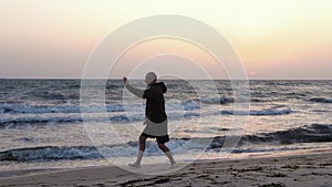Man training Chinese martial art Taijiquan at sea beach, evening sky background
