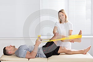 Man Training With Exercise Band Assisted By Physiotherapist