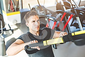 Man training with fitness straps in the gym. Sportsman exercising her muscles sling or suspension straps.