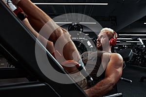 Man training legs in the simulator. young man doing exercises on his legs in the gym to music in headphones