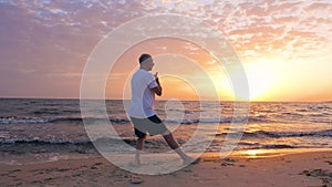 Man training martial art Taijiquan on sea beach and evening sunset landscape