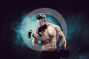 Man training muscles with dumbbells in studio on dark background with smoke.