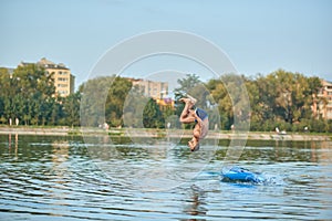 Man training on paddle board, jumping into water head down at city lake.