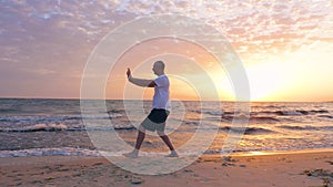 Man training Taijiquan during morning sunrise in sky on sea beach