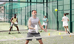 Man training to play tennis on the padel court outdoor. Athletes training in background