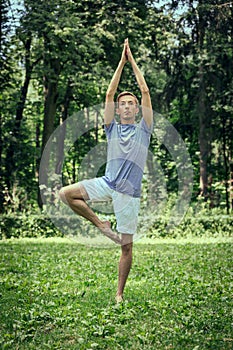Man training yoga in tree pose in park