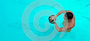 Man trains in pool. View from above on a ailetic male swimmer swimming in the blue clear water wearing goggles for