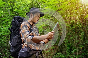 Man traveler with backpack and map searching directions in the forest