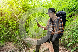 Man traveler with backpack and map searching directions in the forest