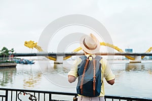 Man Traveler with backpack visiting in Da Nang. Tourist sightseeing the river view with Dragon bridge at love lock bridge.