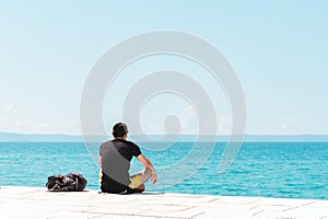 Man traveler backpacker sitting on the seashore looking into the ocean