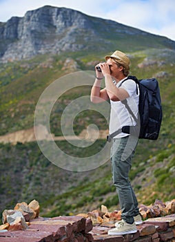 Man, traveler and binoculars with backpack for sightseeing, outdoor travel or hiking on mountain in nature Young male