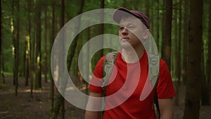 Man traveler in a cap and with a backpack walks through the dark forest, tracking to the camera