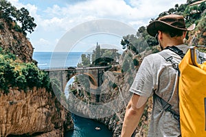 The man traveler enjoys a wonderful view of the beach and the stone bridge. a kangaroo leather cowboy hat. Yellow Waterproof bag.