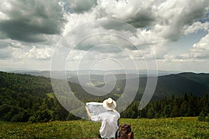 Man traveler exploring map and sitting on top of sunny hill on b