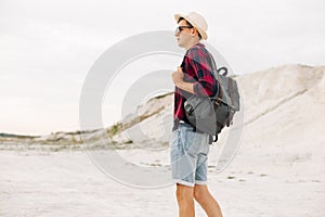 Man traveler in a hat and with a backpack walks along a mountain road, man travel hiking in the Scandinavian mountains