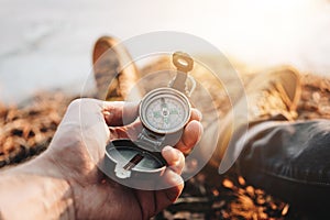 Man traveler hold compass in hand on background legs in hiking boots. Blurred background