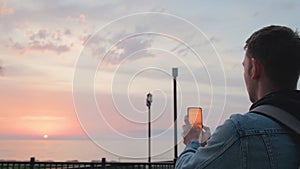 Man traveler photographing sea sunset using camera on his mobile phone. Caucasian guy taking photo on smartphone while