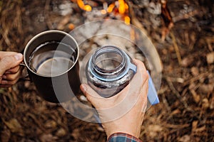 Man traveler pours water from a bottle into a metal mug.