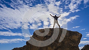 Man traveler with raised hands standing on a rock. Concept of extreme sport and active life