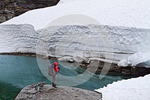 Man traveler in red jacket stands on a rock near the glacier