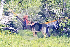 Man traveler is relaxing in hammock and playing with his dog