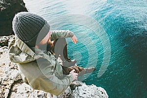 Man traveler sitting on cliff alone thinking above deep sea