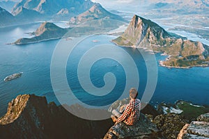 Man traveler sitting on the edge of mountain cliff in Norway alone hiking in mountains outdoor active healthy lifestyle