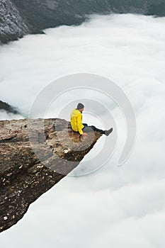 Man traveler sitting on Trolltunga rocky cliff edge