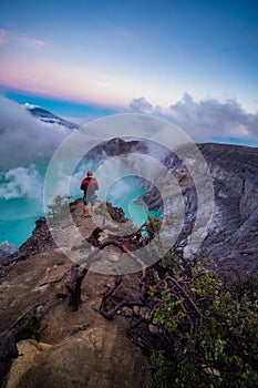 Man traveler standing on edge of crater Ijen volcano with colorful sky at morning