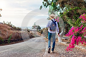 Man traveler walks along road in Akrotiri village on Santorini island Greece. Tourist backpacker admires flowers